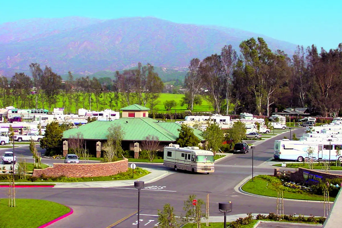 A Class A motorhome driving into Pechanga RV Resort in Temecula, with rows of RVs and green hills behind