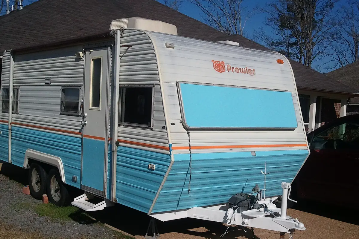A 1983 Prowler travel trailer with fresh white and blue paint parked in a driveway