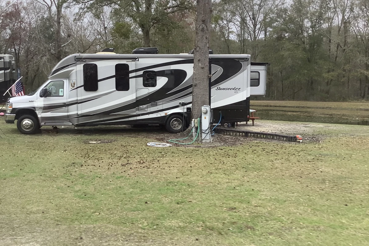 A silver and black Forest River Sunseeker Class C motorhome with its slide out open, parked at a grassy campsite with water and power hooked up