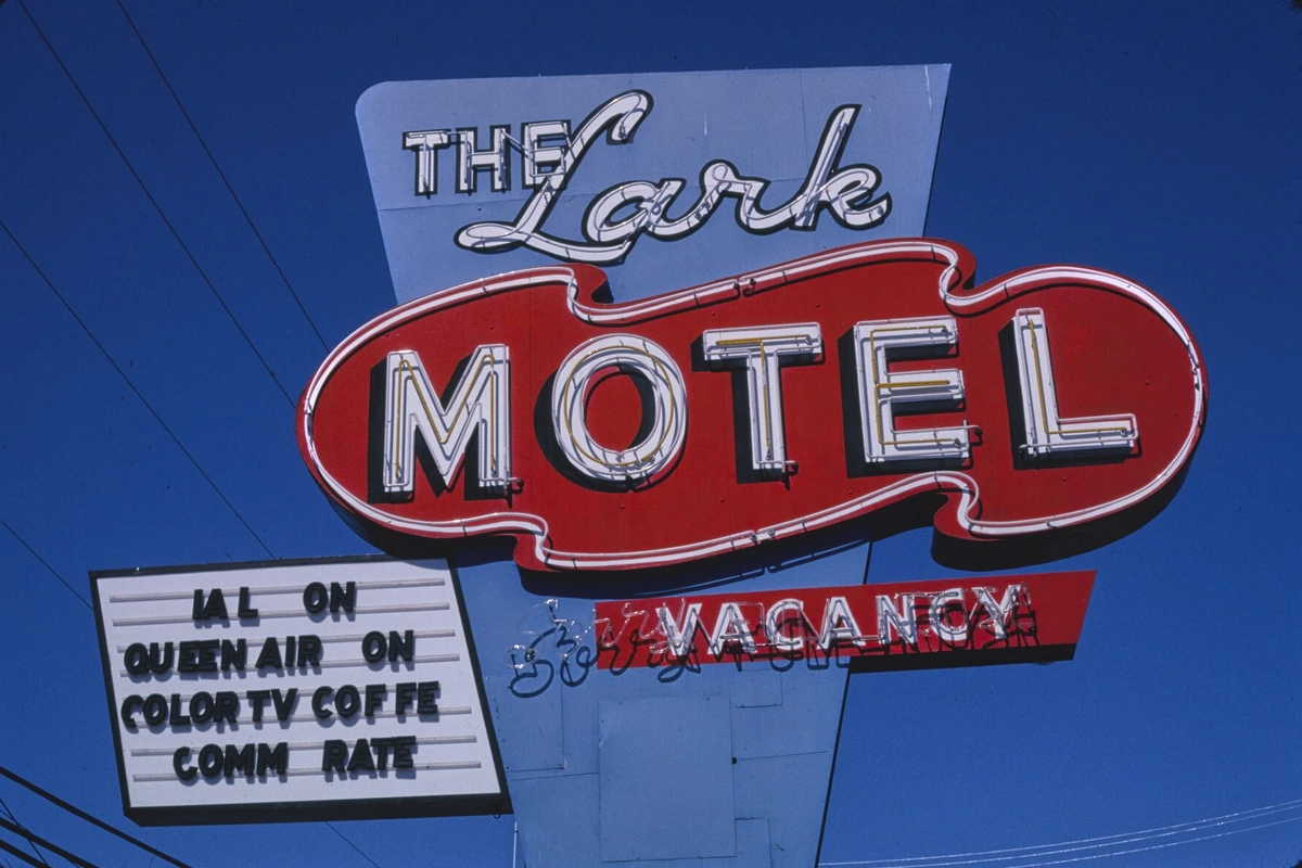 A red and white neon sign reading The Lark Motel with a Vacancy sign and a letter board under a deep blue sky
