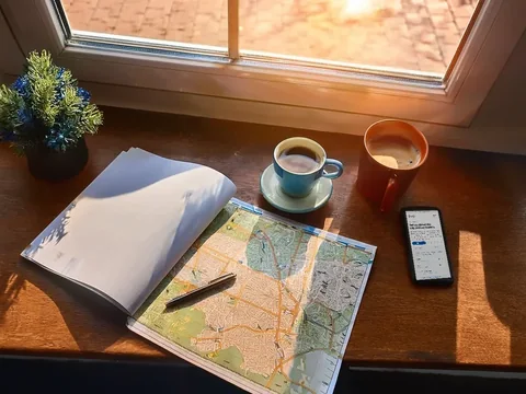 A paper map, a phone and a coffee on a kitchen table at the start of planning a trip